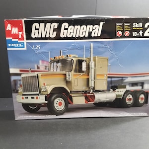 Puede incluir: Una caja de maqueta para un camión GMC General. La caja es azul y blanca con una imagen de un camión de color beige en la parte delantera. La caja dice "Skill 2 10+"
