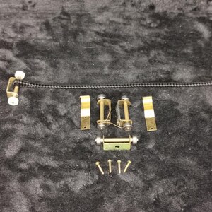 May include: A set of gold-toned metal hardware for a window blind or curtain. The set includes two rollers, two brackets, a connecting bar, and four screws.