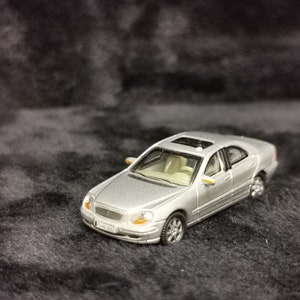 Könnte beinhalten: Ein silbernes Spielzeugautomodell einer Mercedes-Benz S-Klasse Limousine. Das Auto hat ein Schiebedach und steht auf einer dunkelgrauen Oberfläche.
