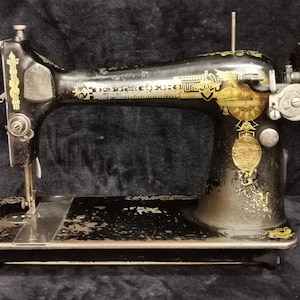 Op de afbeelding: Een zwarte vintage naaimachine met gouden accenten en decoratieve details. De machine heeft een handwiel en een naald.
