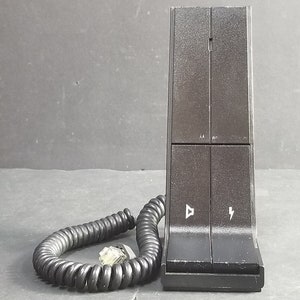 Könnte beinhalten: Schwarze Telefonbasis mit einem Spiralkabel und einem Stecker. Die Basis hat zwei Tasten mit Symbolen für Lautstärke und Blitz.