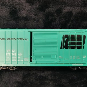 Puede incluir: Un modelo de vagón de mercancías verde turquesa con las palabras "Penn Central" y "PC 272 747" impresas en el lateral. El vagón tiene un gran logotipo negro "ND" en el lateral.