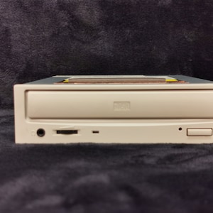 May include: A beige external CD-RW drive with a black front panel. The drive has a headphone jack, a memory card slot, and a button to eject the disc.