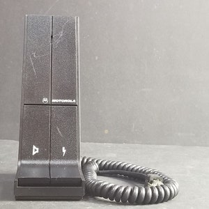 Könnte beinhalten: Eine schwarze Motorola Ladestation mit einem Spiralkabel. Die Ladestation hat zwei Knöpfe, einen mit einem Lautsprecher-Symbol und den anderen mit einem Blitzsymbol.