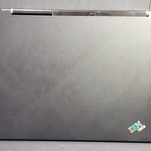 May include: A closed black laptop with a matte finish. The laptop has a silver hinge and a small ThinkPad logo in the lower right corner. An antenna extends from the top.