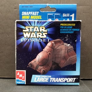 May include: A box for a Star Wars Episode I Trade Federation Large Transport snap-fast model kit. The box is blue and features a picture of the vehicle. The text on the box reads "Star Wars Episode I Trade Federation Large Transport".