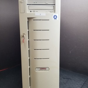 Peut inclure: Un serveur Compaq Proliant 1500 beige avec une clé dans la serrure. Le serveur possède un lecteur de CD-ROM, un lecteur de disquette et un autocollant avec le texte "CA-MPVM-GEN01-T".