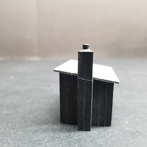 Pode incluir: Uma pequena casa modelo preta com um telhado branco e uma chaminé preta. A casa é feita de madeira e tem um design simples.
