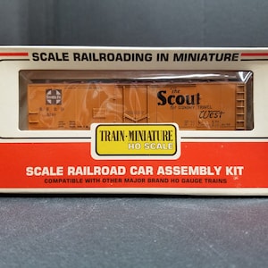 May include: A box for a HO scale model railroad car assembly kit. The box features a picture of a brown boxcar with the words "The Scout for Economy Travel West" printed on the side. The box is labeled "Train-Miniature HO Scale".