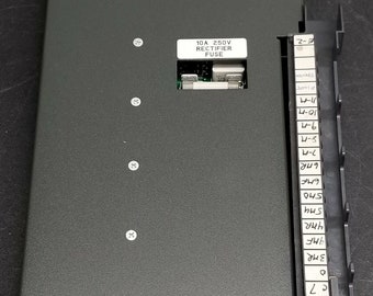 Puede incluir: Un componente electrónico gris oscuro de forma rectangular. Presenta una etiqueta que dice "10A 250V RECTIFIER FUSE". Texto adicional incluye "NOTICE SET JUMPER FOR LAST STATE (LS) OR RESET". El componente tiene múltiples tornillos y un panel lateral con etiquetas.