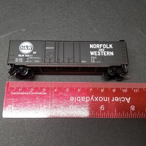 Pode incluir: Vagão de comboio modelo preto com letras brancas que dizem "N&W" e "Norfolk and Western" com uma régua para a escala.