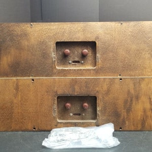 Puede incluir: Dos gabinetes de altavoces de madera con chapa de madera marrón. Cada gabinete tiene un panel rectangular con dos botones y una pequeña abertura rectangular. Los gabinetes están apilados uno encima del otro.