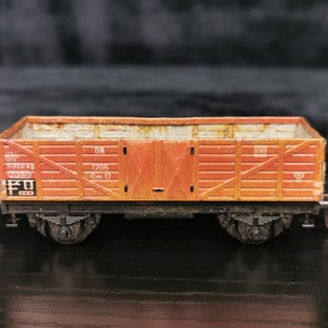 May include: A rusty orange toy train boxcar with black wheels and the text "1205 0m 12" on the side.
