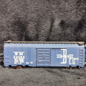 Może przedstawiać: Niebieski model wagonu towarowego z białymi napisami. Wagon jest oznaczony "BM 70056" i zawiera inne informacje o jego pojemności i wadze. Wagon ma białe logo na boku.