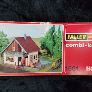 Pode incluir: Uma caixa vermelha e branca com uma casa modelo e árvores. A caixa diz "Faller combi-kit 1561 HO".