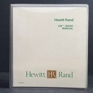 May include: A square, off-white manual titled "GW-BASIC MANUAL" by Hewitt Rand, encased in a clear plastic sleeve. The text is in green, with the company logo featuring "HR" in a brown square. The manual is labeled "S85-527G".
