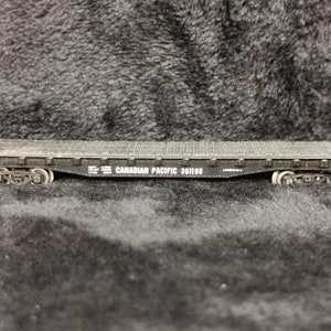 May include: Black model train flatcar with white lettering that reads "CANADIAN PACIFIC 301195".