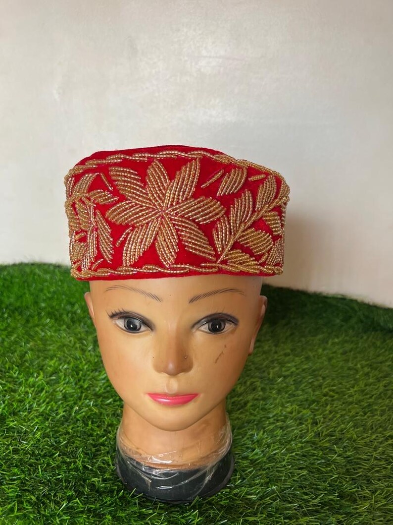 May include: A red hat with gold floral embroidery. The hat is displayed on a mannequin head. The gold embroidery is in the shape of flowers and leaves. The hat is a vibrant red color.