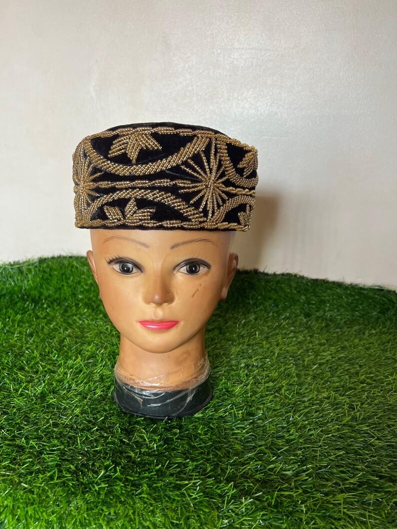 May include: A black velvet hat with gold embroidery. The hat is rectangular with a flat top and a band of gold embroidery around the base. The gold embroidery features a floral design. The hat is displayed on a mannequin head.