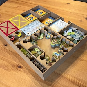 May include: A wooden game organizer with compartments for storing game pieces. The organizer has a brown finish and is filled with various game components, including tiles, cards, and tokens.
