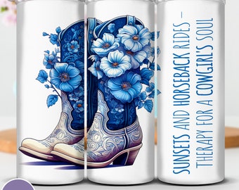 May include: A white tumbler featuring a blue floral design and a pair of cowboy boots. The text on the tumbler reads "SUNSETS AND HORSEBACK RIDES - THERAPY FOR A COWGIRL'S SOUL".
