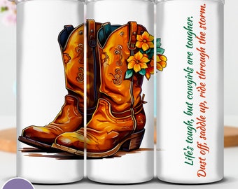 May include: A white tumbler featuring a design of two brown cowboy boots with yellow flowers. The text "Life's tough, but cowgirls are tougher. Dust off, saddle up, ride through the storm." is printed on the tumbler.