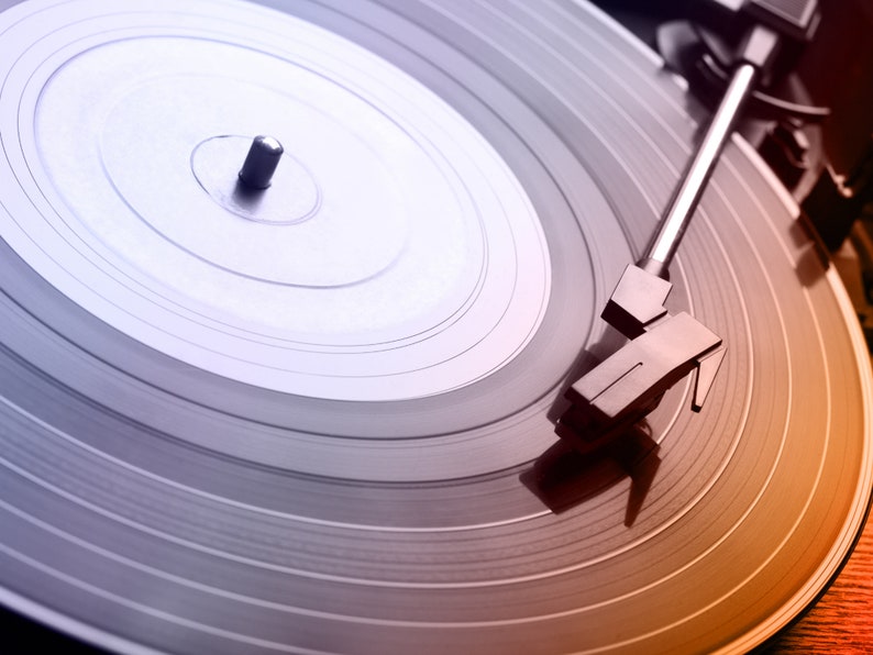 May include: A close-up of a black vinyl record on a turntable. The needle is in the groove and the record is spinning. The turntable is a classic style with a silver tone arm.