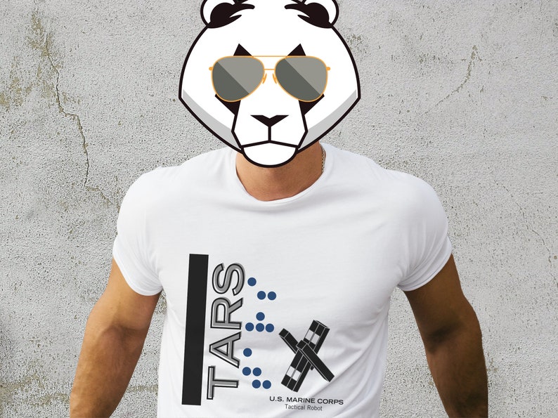 Op de afbeelding: Wit T-shirt met een zwart en grijs grafisch ontwerp met de tekst "TARS" met blauwe stippen en de tekst "U.S. MARINE CORPS Tactical Robot".