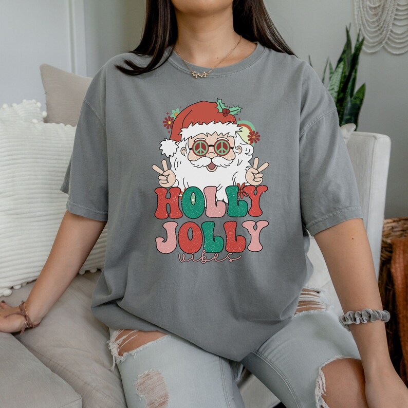 May include: A gray t-shirt with a retro-style illustration of Santa Claus wearing peace sign sunglasses and the text "HOLLY JOLLY vibes".