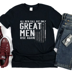 Puede incluir: Camiseta negra con un gr&aacute;fico blanco desgastado que dice "All men fall but only great men rise again" con un dise&ntilde;o de bandera estadounidense desgastado y el texto "Proverbs 24:16".