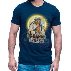 May include: Navy blue t-shirt featuring an illustration of St. Brother Teresa with a yellow halo. The graphic includes the text "ST. BROTHER TERESA" in a stylized font. The shirt is a classic crew neck style.