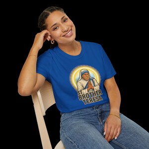 May include: A royal blue t-shirt featuring a graphic of St. Brother Teresa with a halo. The text "ST. BROTHER TERESA" is printed below the image. The shirt is being worn by a person.