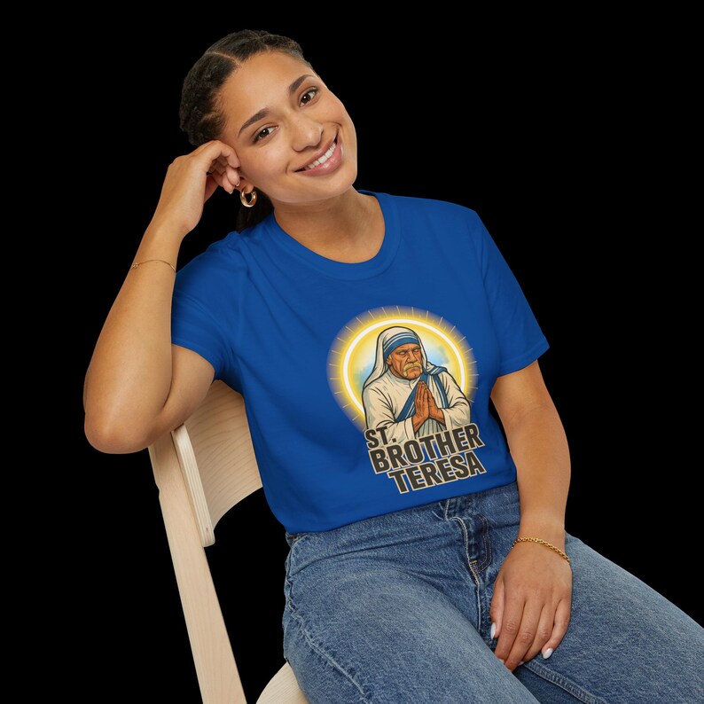 May include: A royal blue t-shirt featuring a graphic of St. Brother Teresa with a halo. The text "ST. BROTHER TERESA" is printed below the image. The shirt is being worn by a person.