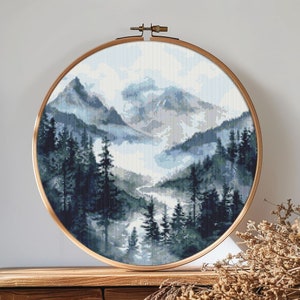 May include: A round embroidery hoop with a cross-stitch design of a misty mountain landscape. The mountains are blue and gray, with a river winding through the valley. The trees are dark green and blue.