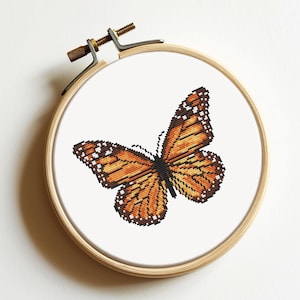 May include: A cross-stitch embroidery of an orange butterfly on a white background, framed in a wooden hoop.