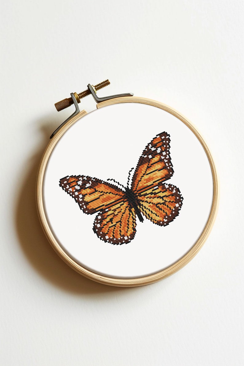 May include: A cross-stitch embroidery of an orange butterfly on a white background, framed in a wooden hoop.