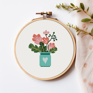 Może przedstawiać: Obręcz do haftu krzyżykowego z wzorem niebieskiego słoika z białym sercem, wypełnionego różowymi i czerwonymi kwiatami z zielonymi liśćmi.