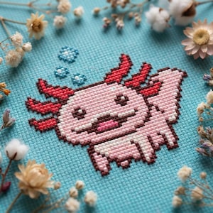 May include: A cross-stitch of a pink axolotl with red gills and a smiling expression, set against a light blue background. The axolotl is surrounded by small blue bubbles and dried flowers. The craftwork is detailed and colorful.