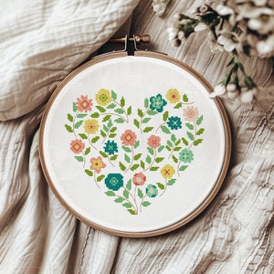 May include: A cross-stitch embroidery hoop with a heart-shaped design of colorful flowers and leaves. The flowers are in shades of pink, yellow, blue, and green.