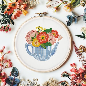 May include: A cross-stitch embroidery hoop with a blue and white striped teapot filled with pink, red, and yellow flowers.