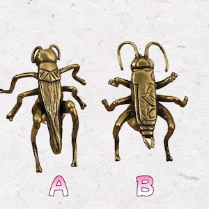 May include: Two brass insect figurines, labelled A and B, are displayed against a textured, off-white background. The detailed insects have six legs, antennae, and intricate body patterns. The figurines are likely decorative items.