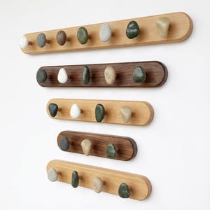 Op de afbeelding: Een verzameling houten kapstokken met afgeronde randen, elk met een rij knopvormige stenen in verschillende kleuren. De kapstokken zijn gemaakt van licht en donker hout, wat een natuurlijke en minimalistische uitstraling creëert.