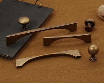 May include: A collection of antique brass cabinet handles and knobs. The hardware is displayed on a brown surface with a dark grey notepad. Some pieces have the text "MADE BY MRTYLE".