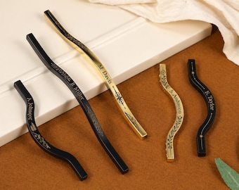 Può includere: Un assortimento di pomelli decorativi per armadi in oro e nero. I pomelli hanno un design curvo con nomi incisi e motivi floreali. I nomi includono "A. Johnson", "B. Miller", "M. Davis", "S. Anderson" e "E. Taylor".