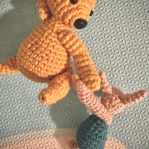 May include: Two crocheted stuffed animals. A larger orange bear with black eyes and a smaller pink bunny with a teal blue skirt.