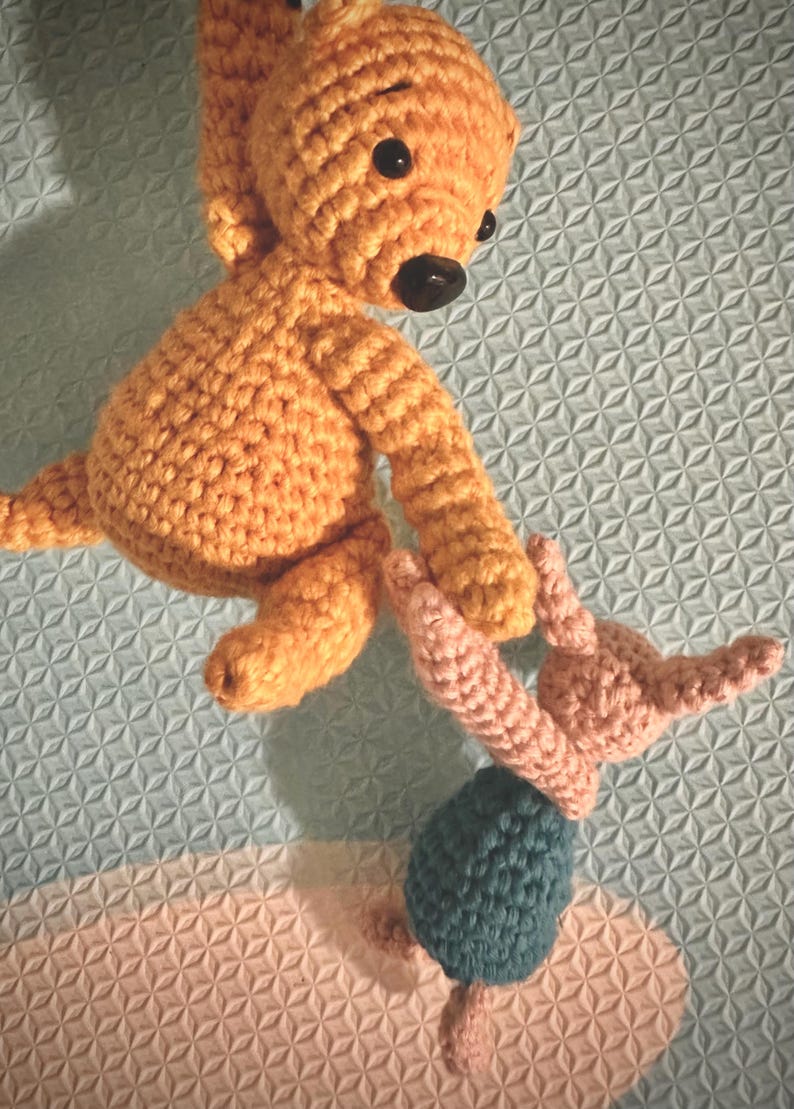 May include: Two crocheted stuffed animals. A larger orange bear with black eyes and a smaller pink bunny with a teal blue skirt.