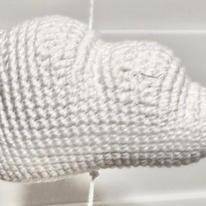 May include: A white crocheted cloud-shaped ornament. The cloud is made with a single crochet stitch and has a textured surface.