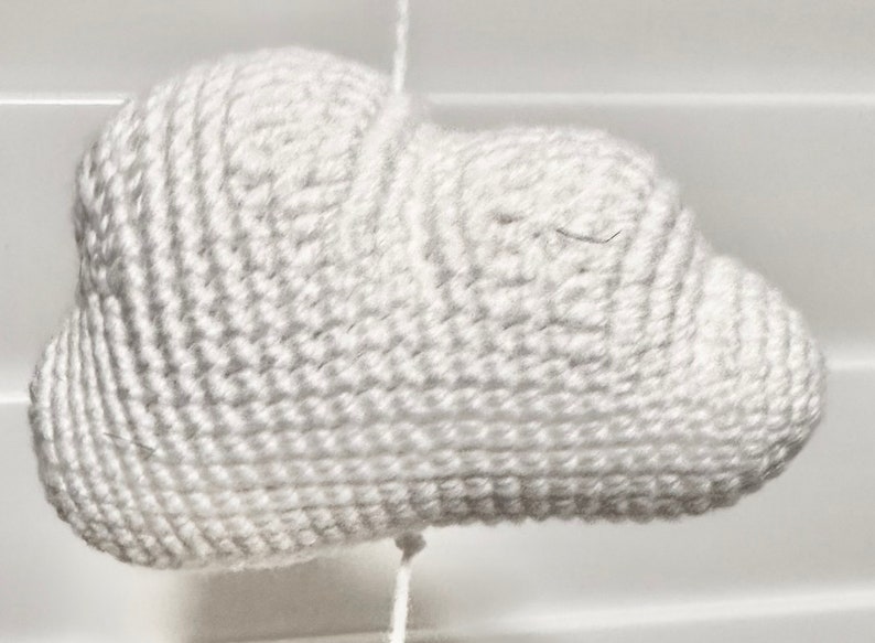 May include: A white crocheted cloud-shaped ornament. The cloud is made with a single crochet stitch and has a textured surface.