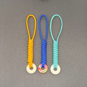 May include: Three keychains with different colored paracord and decorative round charms. The charms are white, multi-colored, and white.