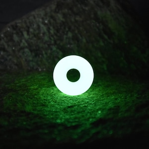May include: A white glowing ring with a hole in the center, sitting on a dark green surface.
